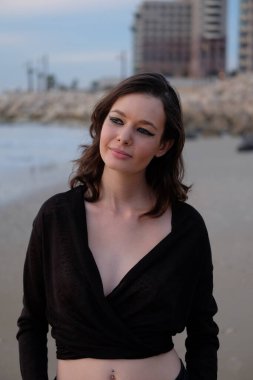 Güzel genç bir kadın gün batımında plajda portresi için poz veriyor.