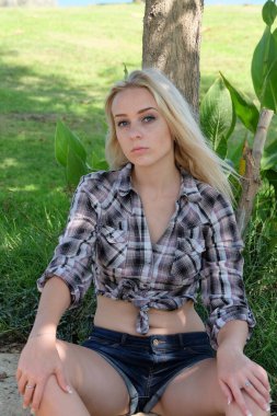 Ekose gömlekli ve parktaki kot şortlu güzel sarışın.