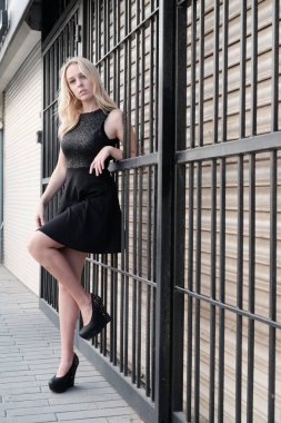 Siyah elbiseli güzel sarışın kadın sokakta poz veriyor.