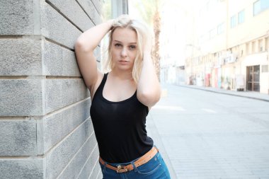 Beyaz gömlekli, kot pantolonlu, tuğla duvarlı genç sarışın kadın..