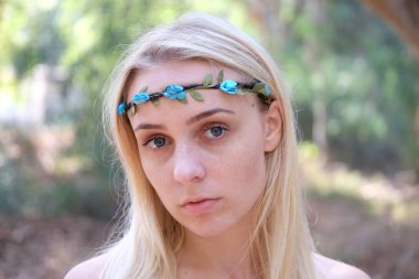 Mavi gözlü ve saçlarında çiçekler olan güzel bir kızın portresi.