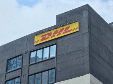 Hong Kong, Çin - 22 Nisan 2025: Kurumsal Ofis Binası Cephesi 'nde DHL Logosu: Uluslararası kurye DHL marka logosu bulutlu bir gökyüzü altında modern gri bir iş binasının dış duvarında belirgin bir şekilde gösteriliyor.