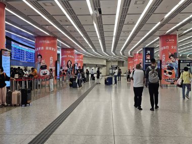 Hong Kong, Çin - 17 Ekim 2023: Batı Kowloon İstasyonu 'nun çağdaş iç kesimlerinde seyahat eden yolcular, belirgin yapısal sütunlar ve ışıklandırma yakınlarındaki açık kalkış işaretleriyle rehberlik ediyorlar..