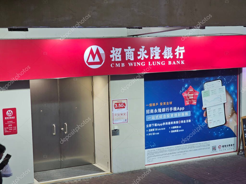 Hong Kong, China - February 5 2025: Brightly lit CMB Wing Lung Bank branch at night, displaying its prominent logo and a large advertisement for mobile app banking services.