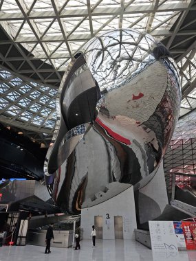 Shenzhen, Çin - 17 Ocak 2025: MOCAPE 'in ikonik' Bulut 'heykeli modern müze alanını keşfeden ziyaretçilerle birlikte geniş geometrik tavan penceresini yansıtıyor.