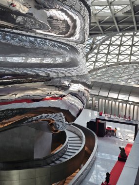 Shenzhen, Çin - 17 Ocak 2025: MOCAPE 'in ikonik' Bulut 'heykeli modern müze alanını keşfeden ziyaretçilerle birlikte geniş geometrik tavan penceresini yansıtıyor.