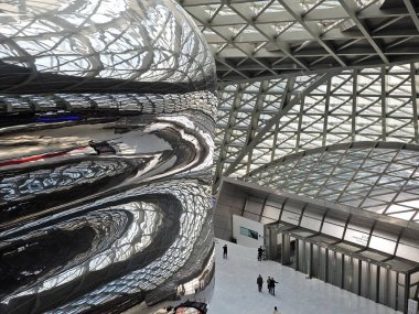 Shenzhen, Çin - 17 Ocak 2025: MOCAPE 'in ikonik' Bulut 'heykeli modern müze alanını keşfeden ziyaretçilerle birlikte geniş geometrik tavan penceresini yansıtıyor.