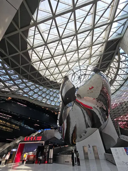 Shenzhen, Çin - 17 Ocak 2025: MOCAPE 'in ikonik' Bulut 'heykeli modern müze alanını keşfeden ziyaretçilerle birlikte geniş geometrik tavan penceresini yansıtıyor.