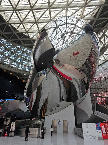 Shenzhen, Çin - 17 Ocak 2025: MOCAPE 'in ikonik' Bulut 'heykeli modern müze alanını keşfeden ziyaretçilerle birlikte geniş geometrik tavan penceresini yansıtıyor.