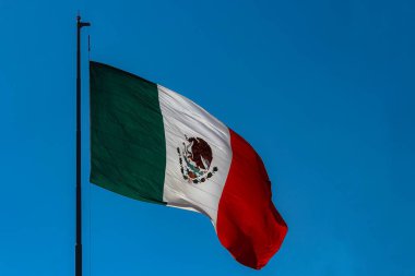 Meksika bayrağı rüzgarla dalgalanıyor ve arka planda masmavi bir gökyüzü 