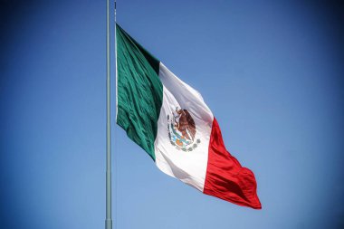 Meksika bayrağı rüzgarla dalgalanıyor ve arka planda masmavi bir gökyüzü 