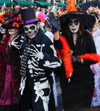 Catrin ve Catrina gibi kılık değiştirmiş bir adamın ön planı, arka planda daha çok insan, Tarih Merkezi 'ndeki Dia de Muertos Geçidi' nde. Mexico Şehri