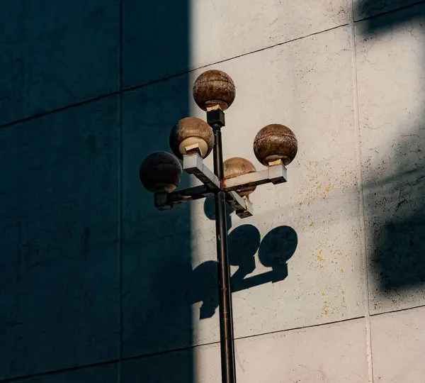 5つのランタンが付いている無駄なランプポストのミニマリストの写真 背景には 太陽の光の一部に照らされた放棄された建物の壁 残りは影です — ストック写真