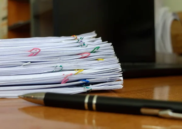 A stack of papers, a pen and a notebook on the desk