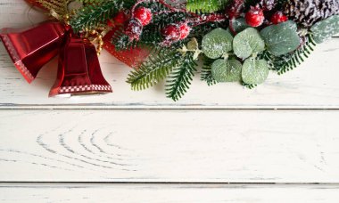 Açık renkli ahşap zemin üzerinde kırmızı çanlar olan Noel ağacı dalı. Alttaki metin için boşluk
