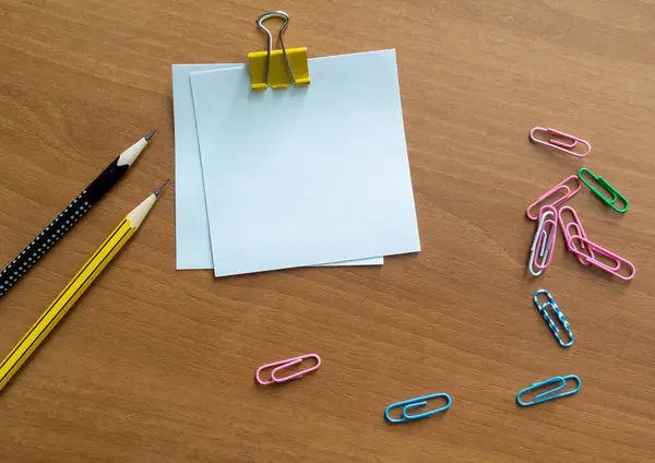 Blank sheets of paperclip notes pencils and paper clips on a wooden desk