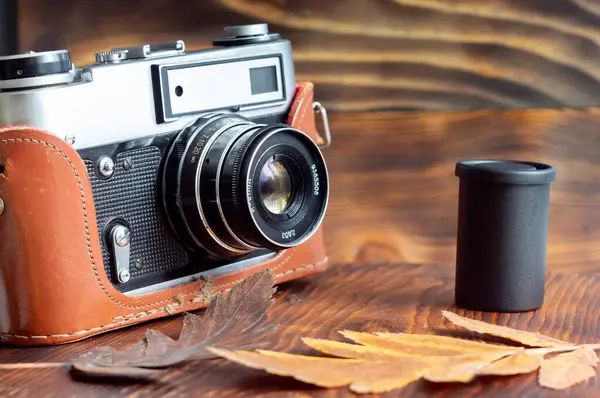 Vintage film camera and film, fall leaves on a wooden background