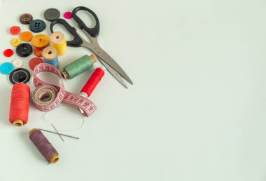 Dikiş dikmek için arka plan. Hafif bir arka planda dikiş malzemeleri. İplik, makas, düğme, mezura, dikiş aksesuarları. Dikiş seti üst görünümü