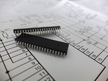 Çeşitli entegre devreler, DIP SOIC TQFP paketlerindeki mikro kontrolörler. Arkasında şematik bir şema var.