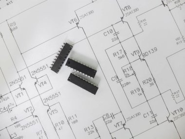 Çeşitli entegre devreler, DIP SOIC TQFP paketlerindeki mikro kontrolörler. Arkasında şematik bir şema var.
