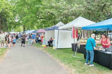 Auburn WA USA, 4 Temmuz 2025 - Parktaki bir festivalde yiyecek ve hediyelik eşya satıyor. İnsanlar parkta bir festival fuarında yürüyorlar..