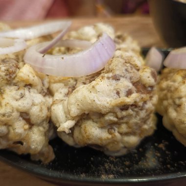 Kızarmış domuz eti ve ahşap masadaki siyah tabakta soğan.