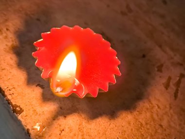 A close-up image of a lit diya (oil lamp) with a red base, casting a warm glow on a textured surface. clipart