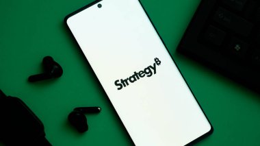 Dhaka, Bangladeş 24 Mayıs 2025: 'Strateji' kelimesini yakınlarda kulaklıklar bulunan yeşil bir arkaplanda gösteren akıllı telefon.