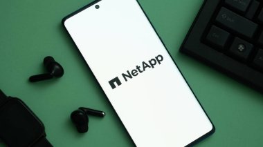 Dhaka, Bangladeş 23 Mayıs 2025: Çevresindeki kulaklıklar ve bir klavye ile NetApp logosu sergilenen yeşil yüzey üzerindeki akıllı telefon.