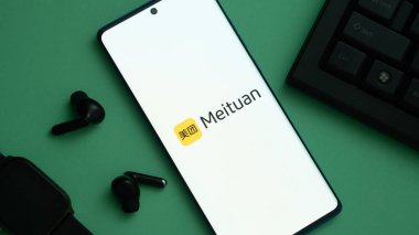 Dhaka, Bangladeş 23 Mayıs 2025: Meituan logosunu yeşil yüzey, kulaklıklar ve klavye yakınında gösteren akıllı telefon.