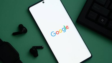 Dhaka, Bangladeş 20 Mayıs 2025: Kulaklıkların yanında Google logosu ve yeşil bir yüzey üzerinde bir klavye gösteren akıllı telefon.