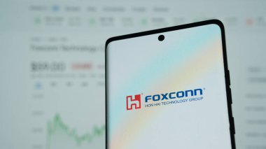 Dhaka, Bangladeş 20 Mayıs 2025: Foxconn logosunun arkasında bulanık bir borsa grafiği bulunan akıllı telefon.