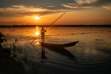 Gün batımında dingin sularda siluet içinde bir balıkçı.