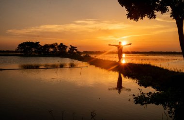 Gün batımında suyun kenarında kutlama yapan biri.