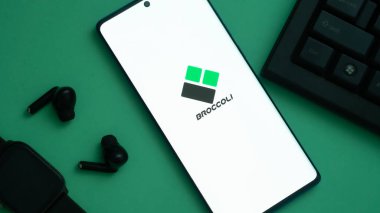 Dhaka, Bangladeş 02 Haziran 2025: Brokoli logosunu gösteren akıllı telefon, kulaklıklar ve yeşil bir yüzey üzerinde bir klavye eşliğinde.