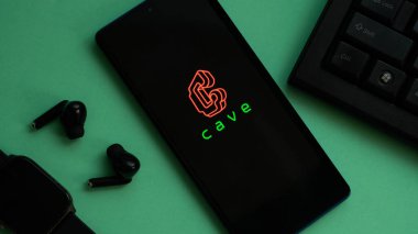 Dhaka, Bangladeş 02 Haziran 2025: Kulaklık ve klavye ile mağara logosunu yeşil arkaplanda gösteren telefon.