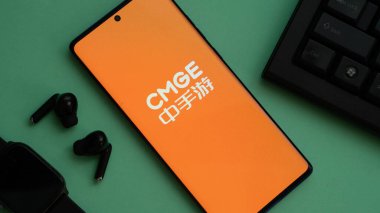 Dhaka, Bangladeş 02 Haziran 2025: Klavye ve kulaklıklı yeşil bir yüzey üzerinde Çince yazılı CMGE logosunu gösteren telefon.