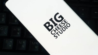 Dhaka, Bangladesh 02 June 2025: Smartphone displaying BIG CHEESE STUDIO logo on white screen over black keyboard.