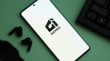 Dhaka, Bangladeş 04 Temmuz 2025: Aksesuarlı yeşil yüzey üzerinde 'GI GAMES' logosunu gösteren akıllı telefon