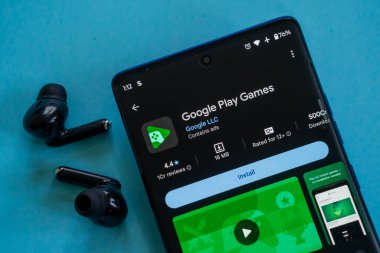 Dhaka, Bangladeş 23 Ağustos 2025: Google Play Games uygulaması mavi bir yüzey üzerinde kulaklık takılı bir telefonda görüntülendi