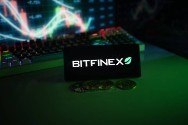 Dhaka, Bangladeş 18 Eylül 2025: Bitfinex ekranı, yeşil neon ışıklarıyla aydınlatılan hisse senedi grafiğinin önündeki paralar