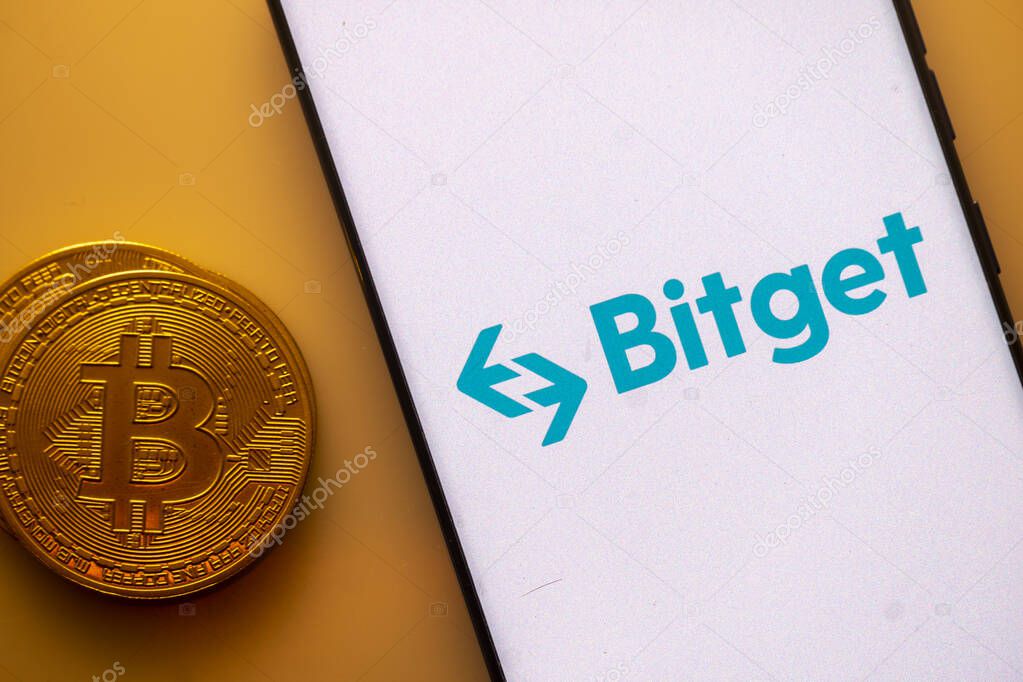 Dhaka, Bangladesh 22 September 2025:Bitget logo on a smartphone screen beside a Bitcoin coin on an orange background