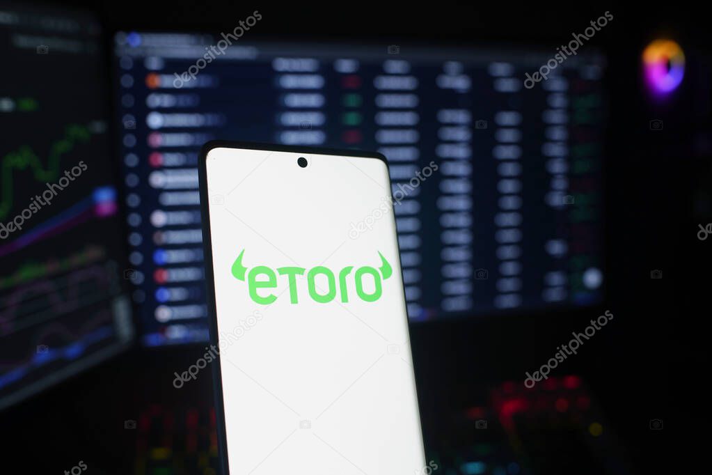 Dhaka, Bangladesh 26 September 2025:Smartphone with eToro logo highlighted against trading screens showing market data