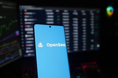 Dhaka, Bangladesh 26 September 2025:Smartphone displaying OpenSea logo with trading screens in the background