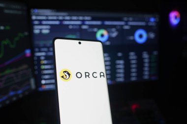 Dhaka, Bangladesh 26 September 2025:Smartphone featuring ORCA logo with trading data on screens behind