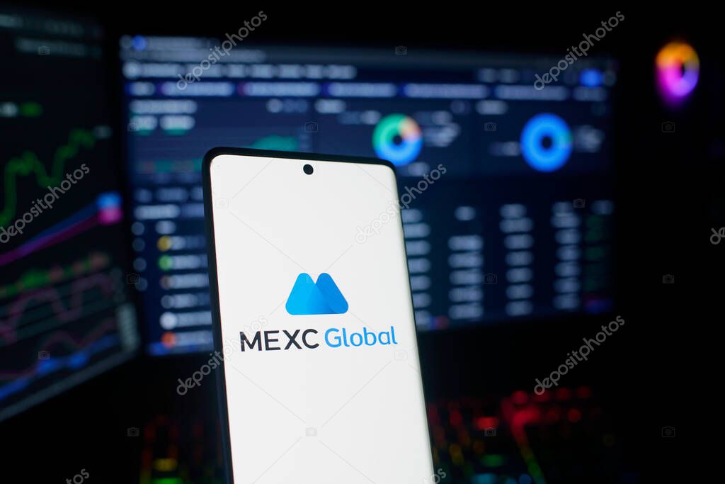 Dhaka, Bangladesh 26 September 2025:Smartphone with MEXC Global logo in front of trading charts on screens