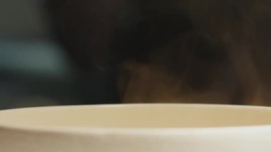 Masanın üzerinde beyaz bir kase çorba var. Kasenin üzerindeki sıcak çorbadan beyaz buhar yükseliyor. Manzarayı kapat. Yüksek kalite 4k görüntü