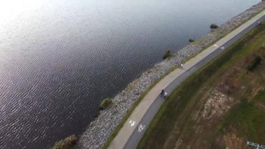 Bir aile güzel bir göl boyunca bisiklet yolu üzerinde bisiklet sürüyor. İHA görüntüsü. Hafta sonu aktivitesi. Yüksek kalite 4k görüntü