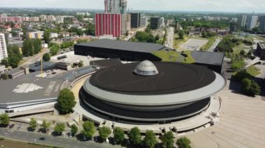 Hava aracı, işlek bir şehirde, gelecekteki gökdelenlerin üzerinde yükselen modern dairesel bir bina sergiliyor.