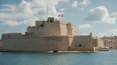 Malta 'daki tarihi bir kalenin resimli kıyı manzarası, hafif rüzgarda dalgalanan bir bayrak.